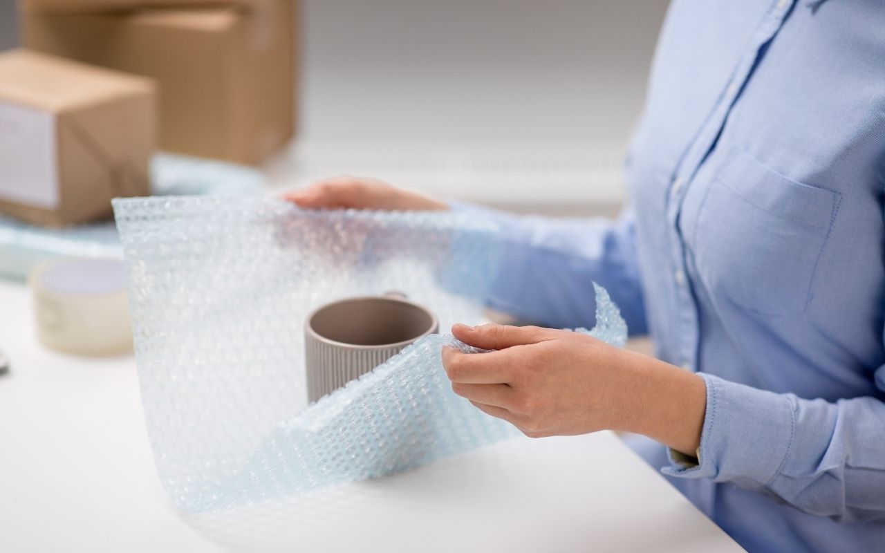 Hands wrapping glassware with bubble wrap for move